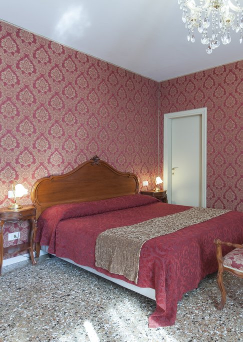 chambre double panoramique avec détail du lit et murs en damas rouge